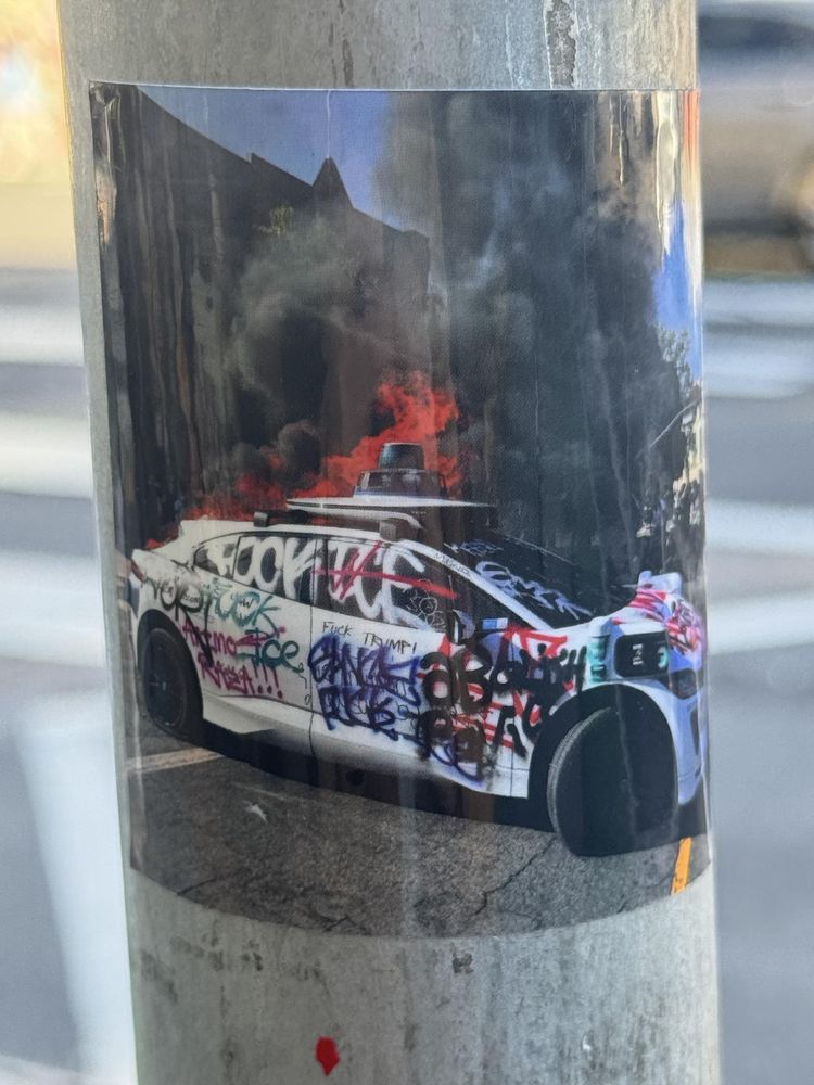 A sticker with a photo of a flaming Waymo on it. I believe this photo was taken during anti-ICE protests in L.A. earlier this year. 