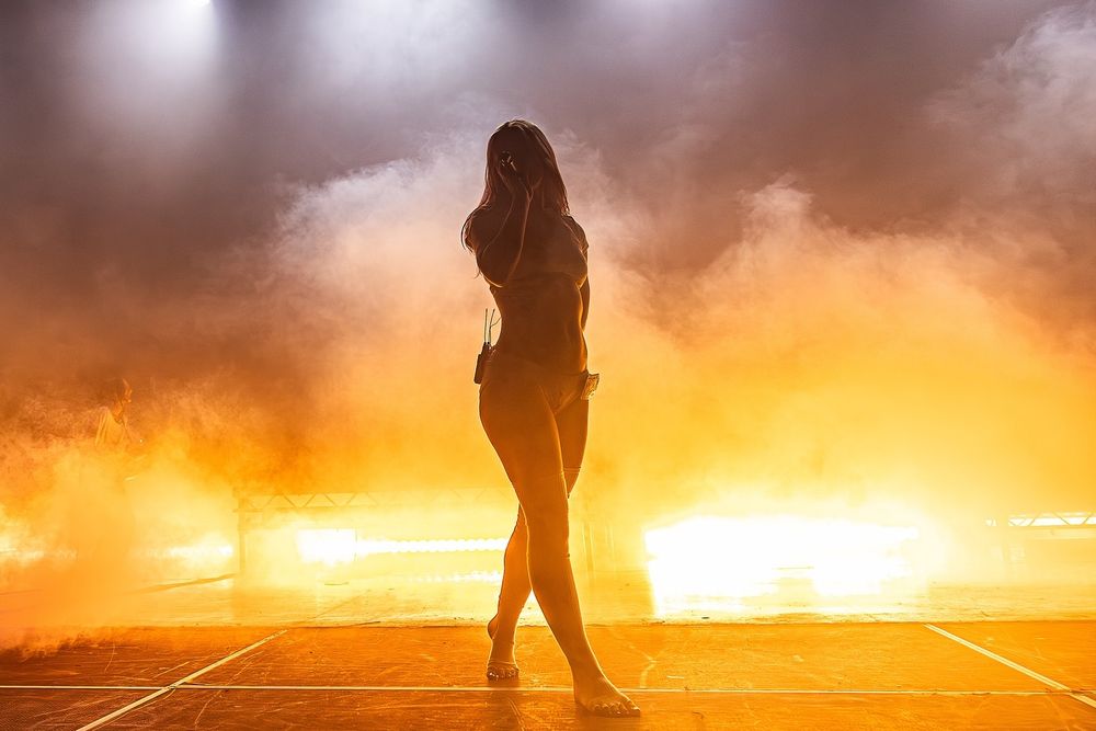 Photo of Rhian Teasdale performing live. Behind her smoke and orange lights. She is wearing white bra and underwear and these socks that have toe holes. She is crazy hot.