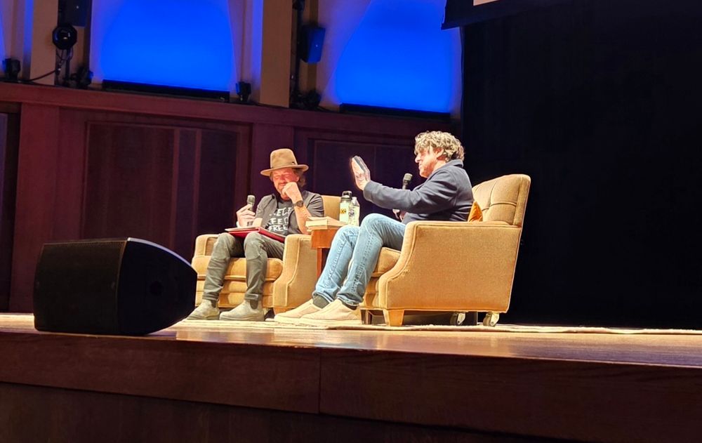 A photo of Cameron Crowe on stage in a comfy rolling chair at Benaroya Hall in Seattle, WA, with moderator Eddie Vedder in a matching chair next to him.