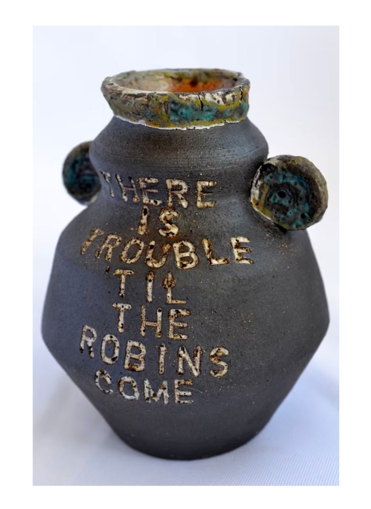 A dark brown ceramic vase stamped with the words, "There is trouble til the robins come." 