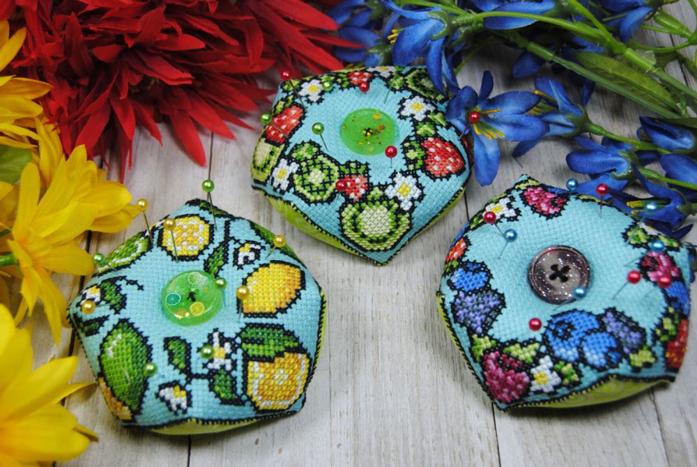 Three fruit-themed cross stitch biscornu used as pin cushions. A Lemon Lime, a Strawberry Kiwi, and a Wildberry design featuring Blueberries, Raspberries, Blackberries, and Strawberries.