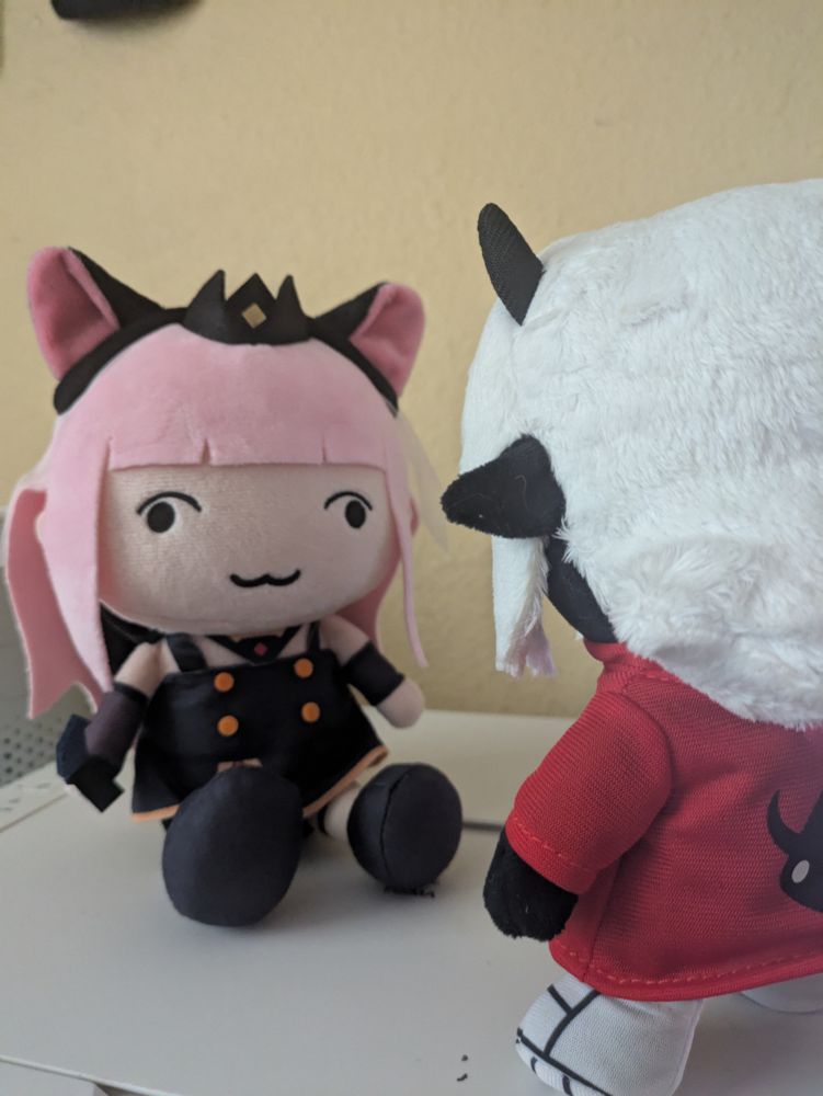a Demondice plush facing a Weird Cat plush (who oddly resembles Mori Calliope)