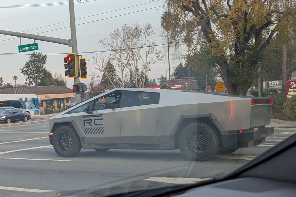 Cybertruck with hazards on sitting at a green light waving cars past