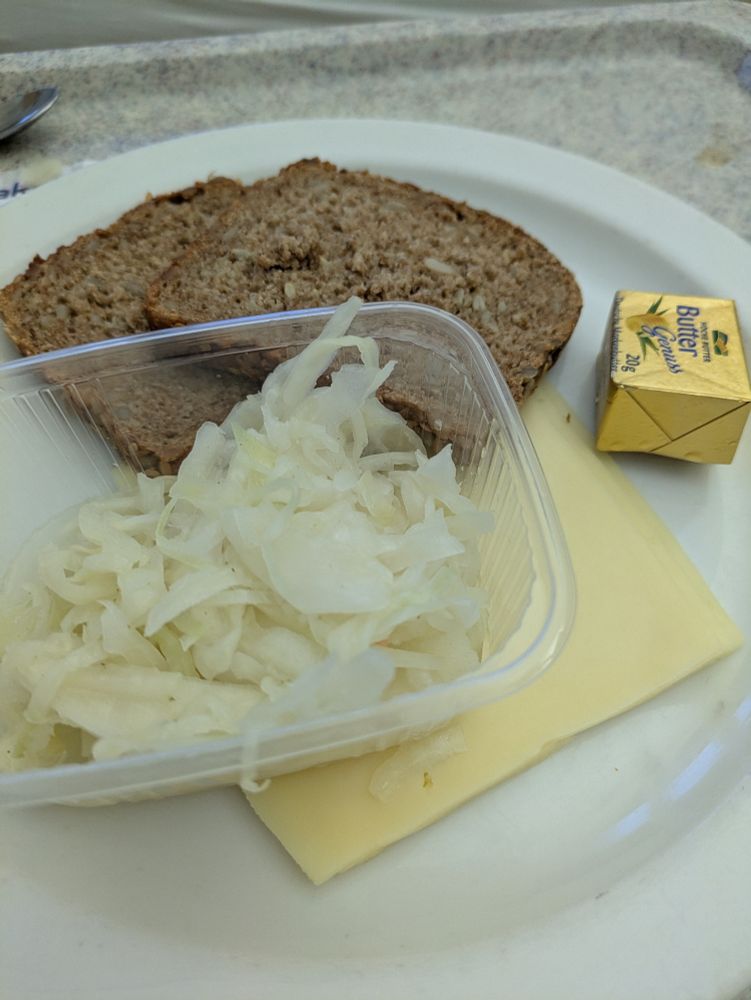 Zwei Scheiben Brot, Käse, Butter und Krautsalat im Plastikschälchen auf einem Teller