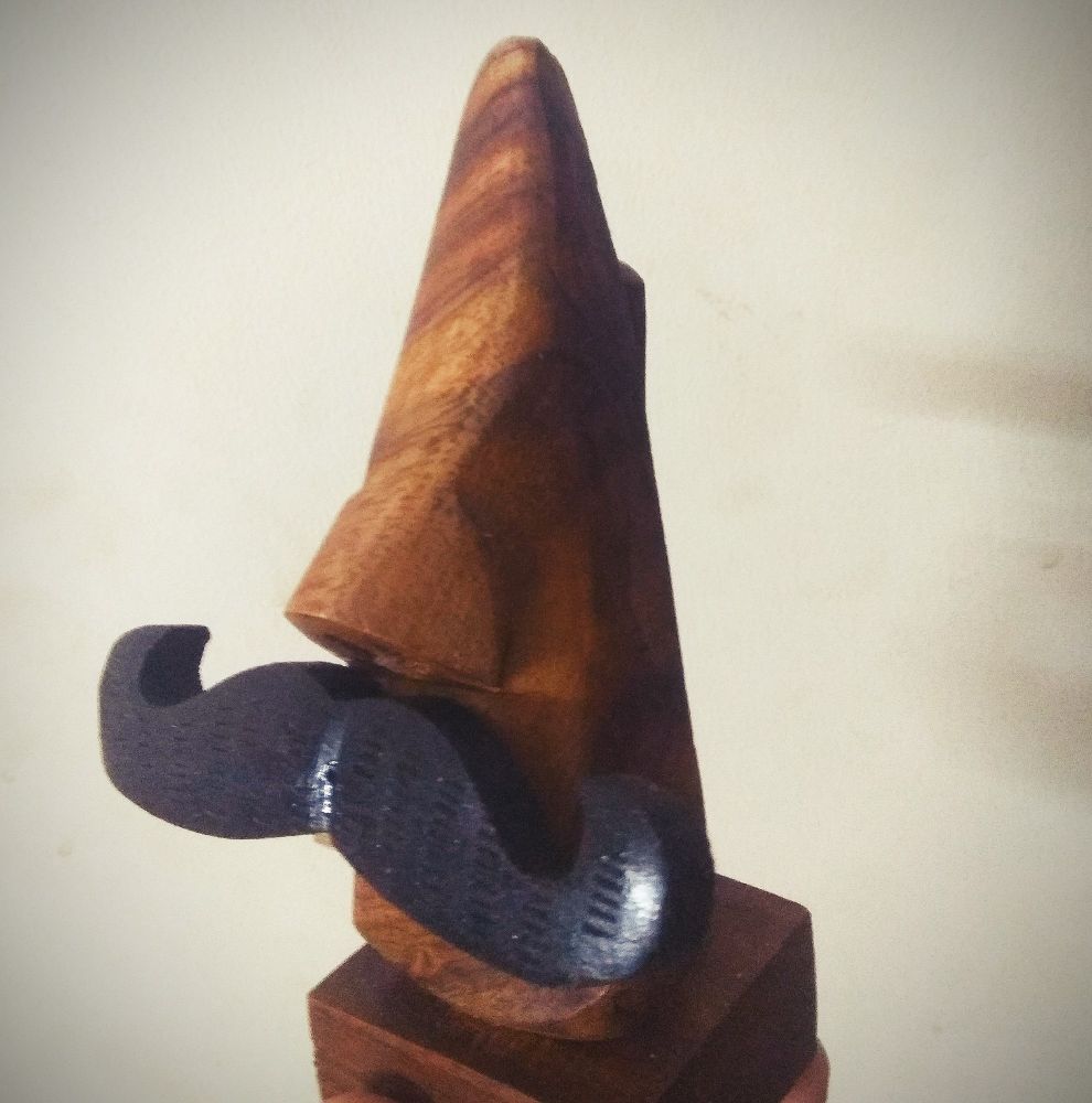 A wooden stand in the shape of a nose with an obnoxiously large fake mustache.