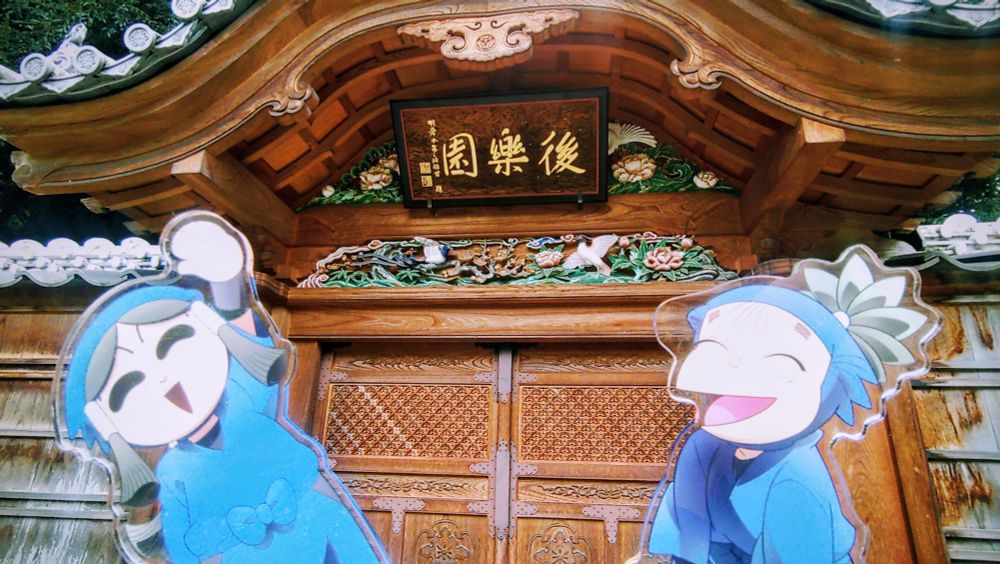 東京で立ち寄った小石川後楽園の門の写真。手前に忍たまのキャラ、時友四郎兵衛と羽丹羽石人のアクスタ。