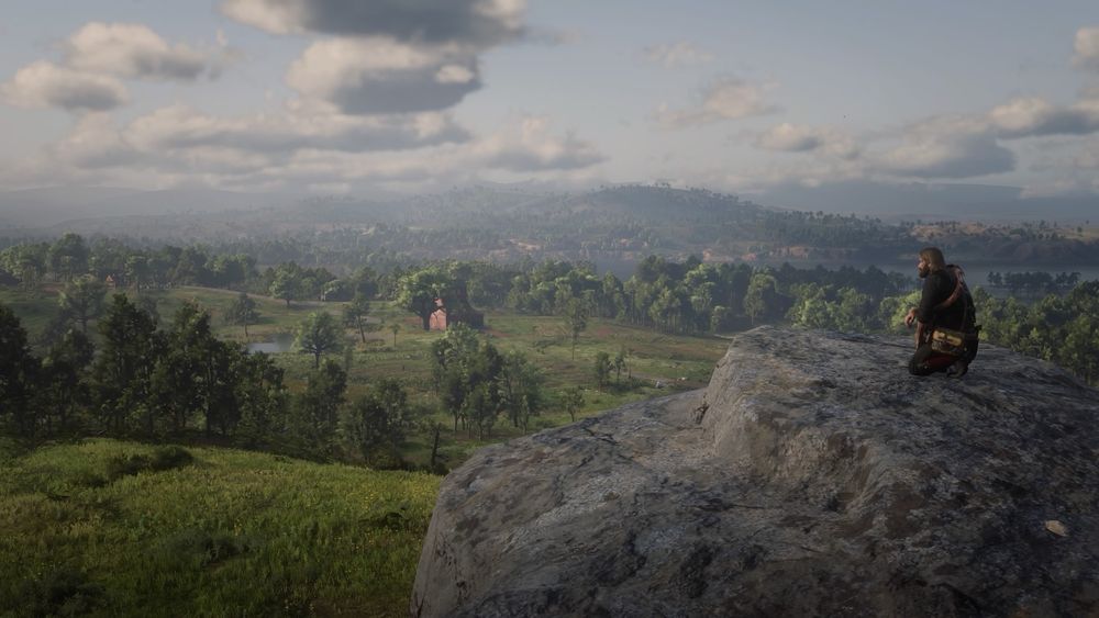 An in game photo of Arthur Morgan from Red Dead Redemption 2. He is kneeling on a cliff overlooking a vast field of trees with a barn in the distance.