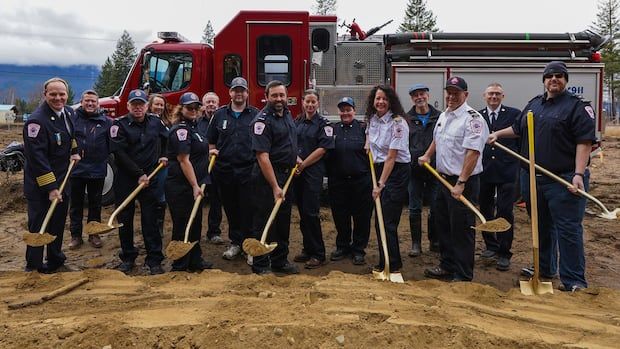 Firefighters hold shovels in front of a firetruck.