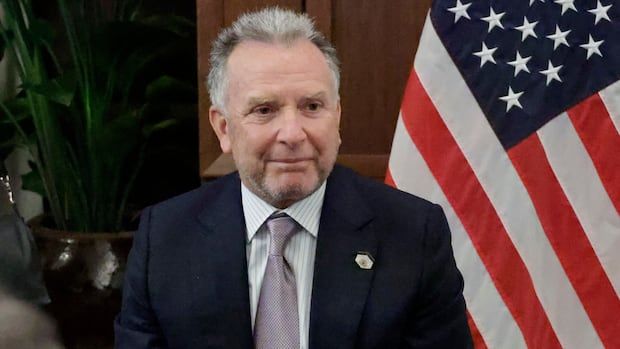 A man in a suit in front of an American flag.
