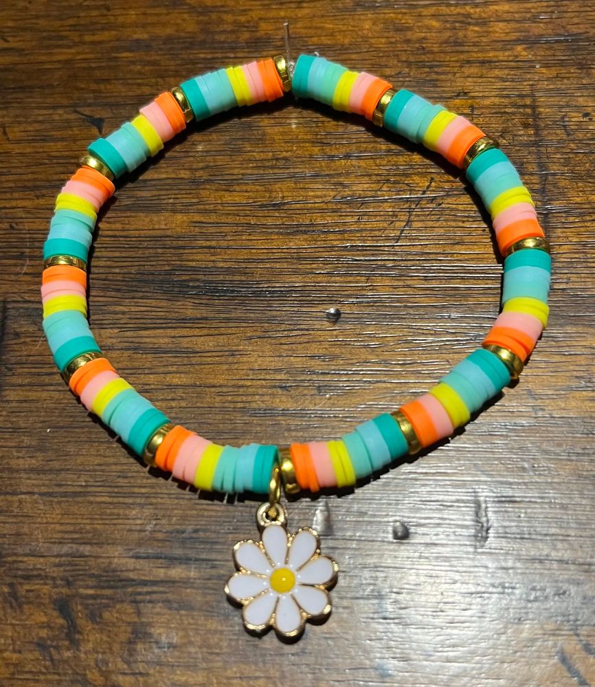 A bracelet lays on a dark wooden background. The bracelet features the colors orange, peach, yellow, light blue, mint, and teal with a daisy charm. 