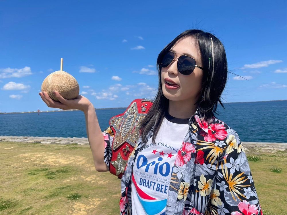 Professional wrestler Saya Kamitani poses in a Hawaiian shirt & sunglasses, holding a coconut in Okinawa 