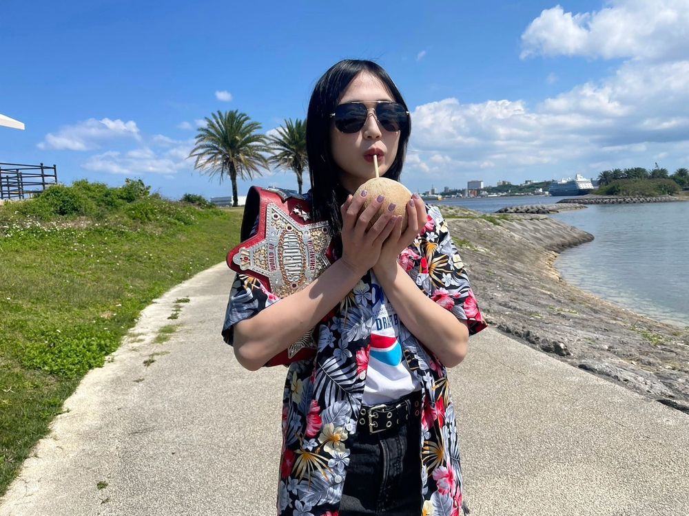 Professional wrestler Saya Kamitani poses in a Hawaiian shirt & sunglasses, sipping from a coconut in Okinawa 