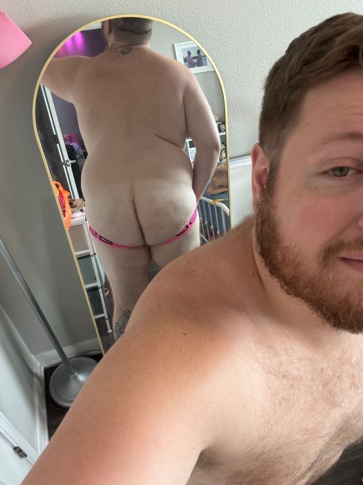 Standing in front of my mirror with my back to it wearing my new neon pink jockstrap showing my fat ass. 