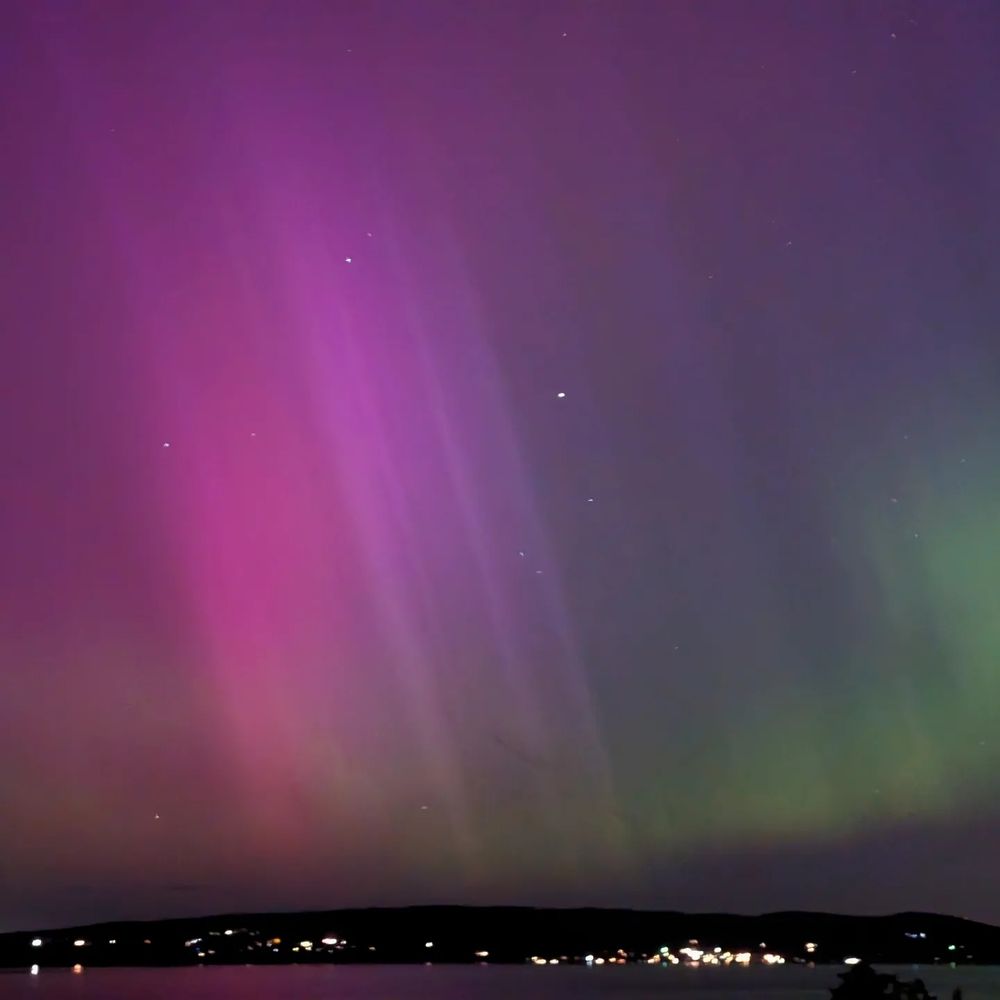 Magenta flash of aurora across the left half of the sky, with subtle green aurora on the lower right. Whidbey Island and Saratoga Passage below.