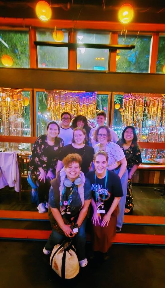 Nine people in a brightly colored restaurant pose for a photo on steps, all smiling widely