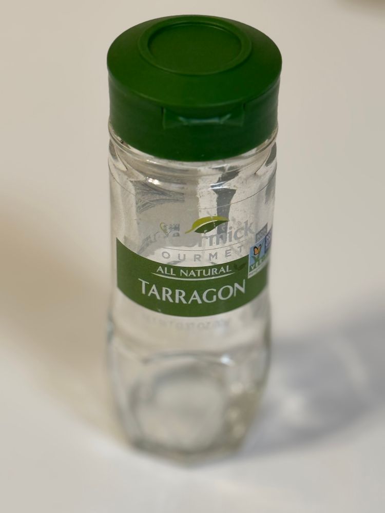 An empty glass bottle with a green label identifying the former contents as dried tarragon.