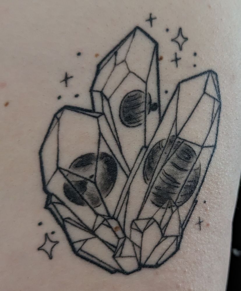 Black and grey crystal tattoo, with objects embedded in them. Earth-like exoplanet on the left, a transiting exoplanet in the middle, and a brown dwarf on the right. Sparkles surround the crystals
