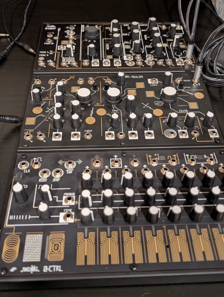 Three Make Noise synthesizers lined up in a row. In front is the 0-CTRL, which is a sequencer with touch plates. Behind it is the Strega, and behind that is the 0-Coast.