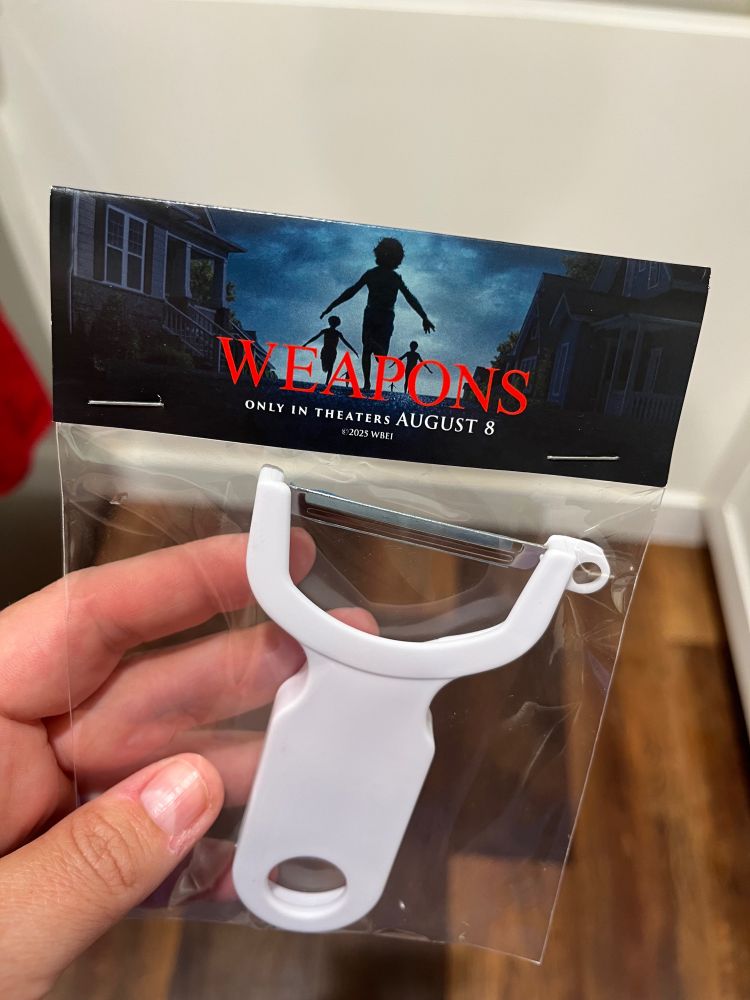 A white plastic WEAPONS branded Y vegetable peeler