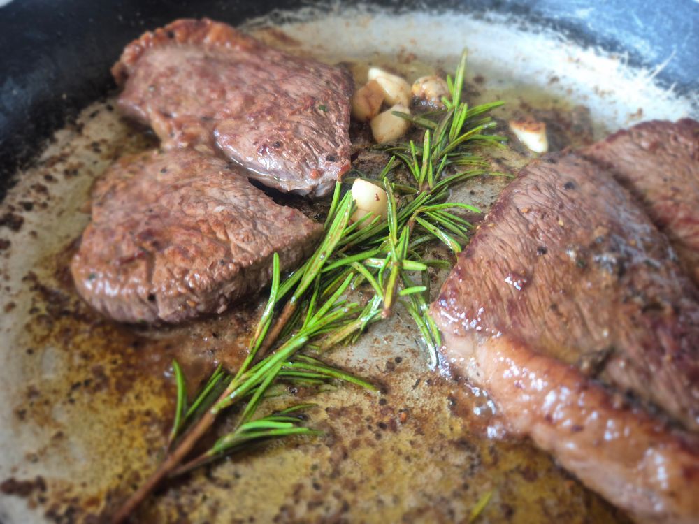 Rump steak cooking in a pan with butter, rosemary, and garlic 