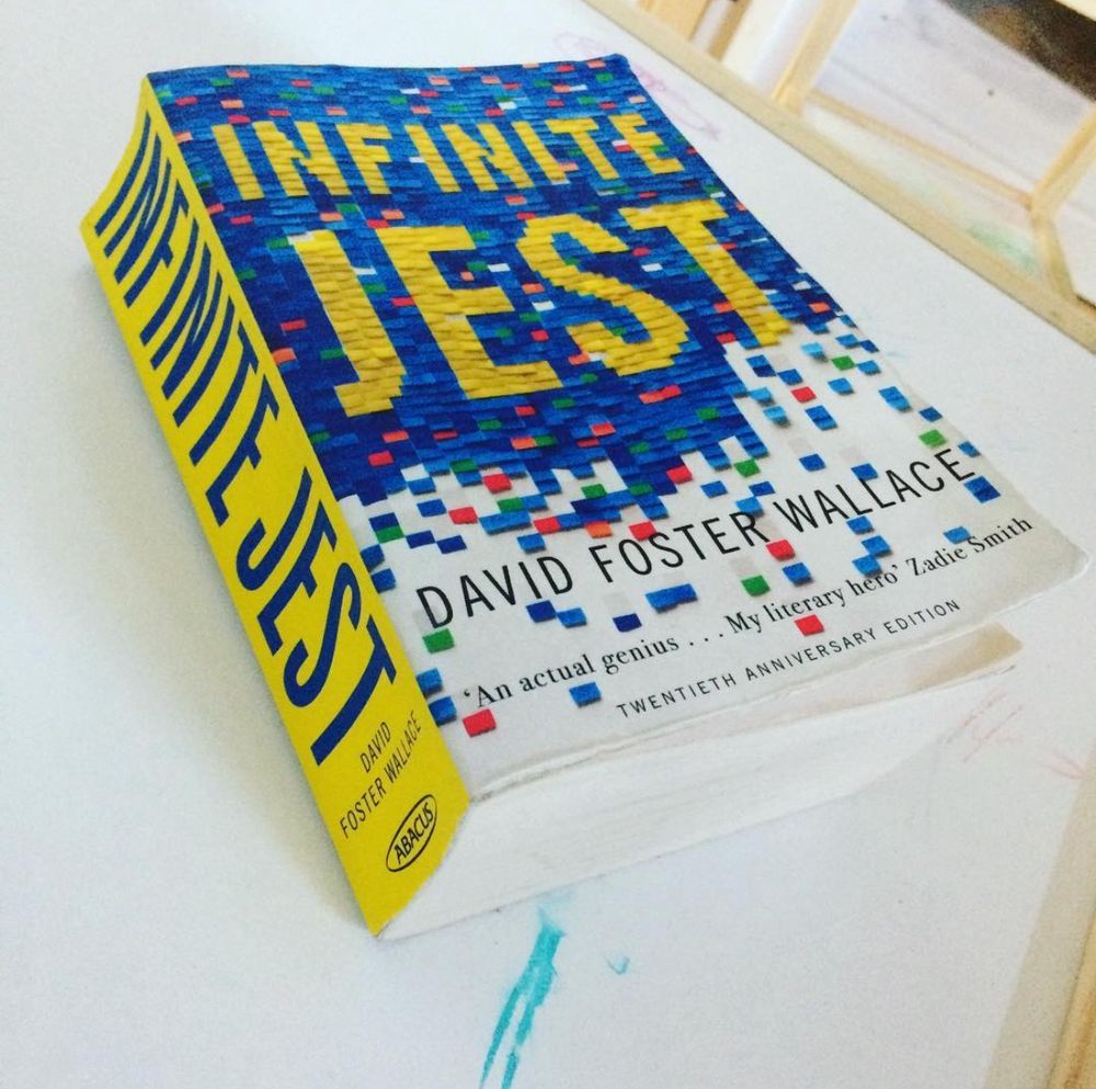 A well thumbed paperback of Infinite Jest by David Foster Wallace placed on a white surface. 