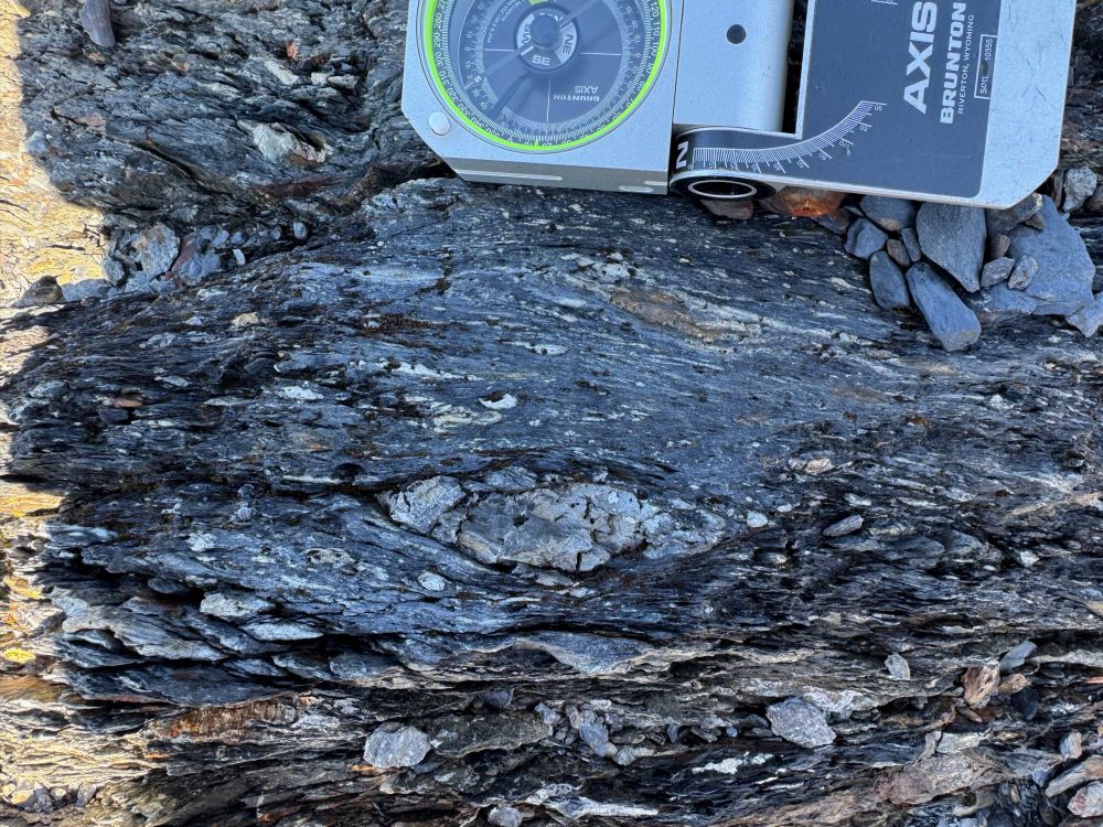 Close-up photo of a rock outcrop with a compass, showing very well-developed block-in-matrix, melange fabric, including lenses of sandstone in a finer matrix. 