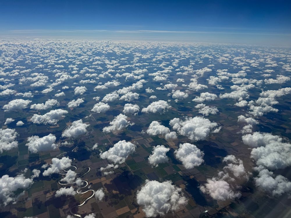 Puffy clouds, meandering river reflecting the sun, and landscape. Taken in September from an airplane window seat high above some midwestern location. 