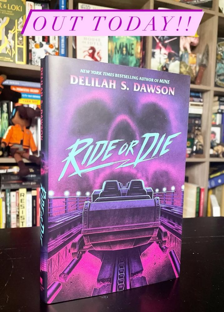 The book RIDE OR DIE is pictured against Delilah's bookshelf. It features a roller coaster on a broken track rolling into a skull cloud and was created by Matt Ryan Tobin. It's got 80s/90s vibes, and you should definitely pick it up today. p.s. There is a ghost crocodile. Don't you love ghost crocodiles? I think we all do.