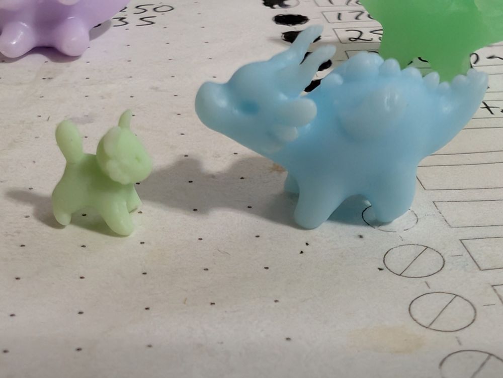 The tiny light green tiger and small pastel blue dragon figurines are situated with their fronts toward each other on top of a notepad