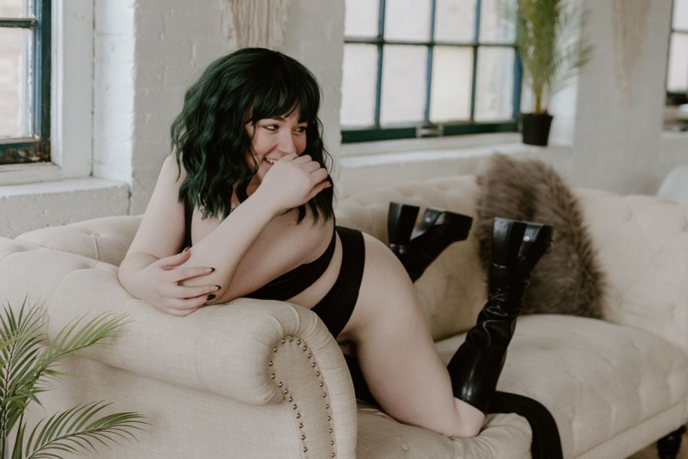 Willow perches across a cozy cream colored couch looking off camera and grinning slyly. 