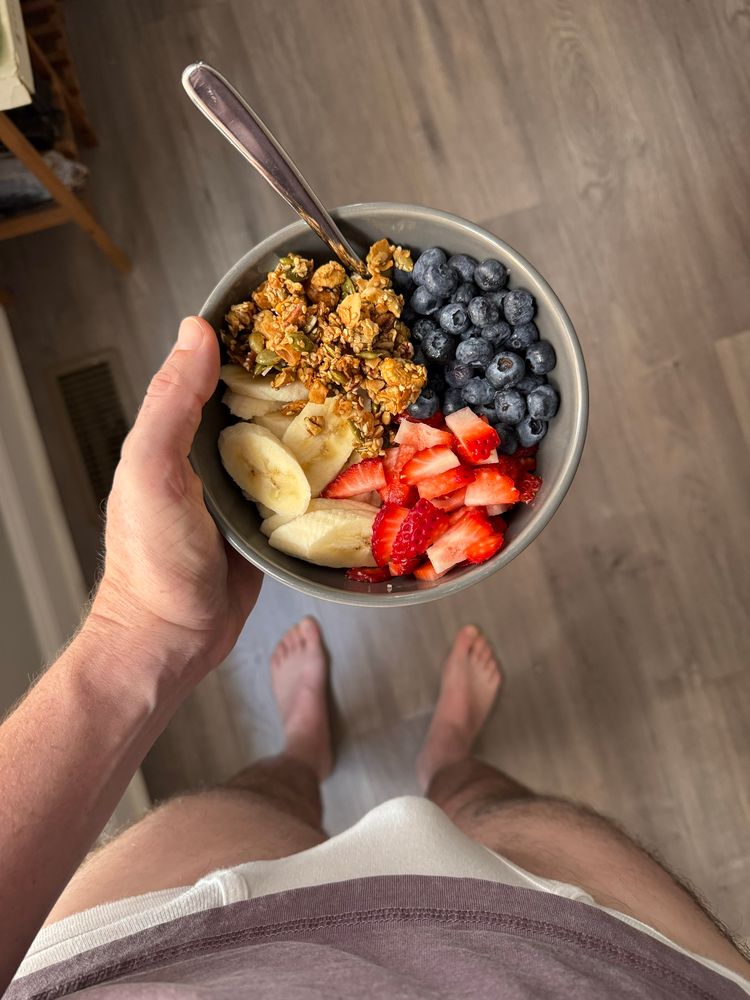 Downward shot of a beautiful bowl of fruit (strawberries, blueberries & banana) & granola over some not-visible chia pudding. You can also see Gray's bulge in white briefs, with his out of focus feet in the background.