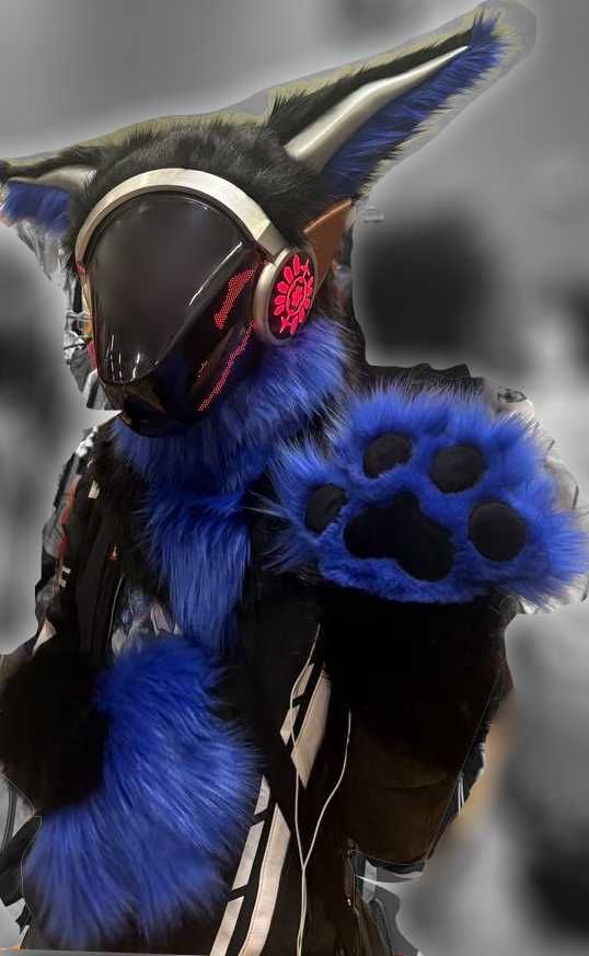 Blue and black furred protogen fursuit partial with RED LEDs and silver and bronze painted plastics as to be metallic. Facing viewer paw waving, grey background.