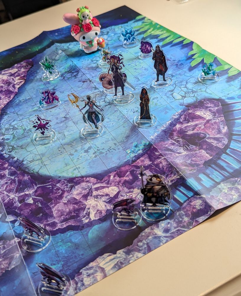 A battle may with a pink Sanrio My Melody character and a number of acrylic standee miniatures, including floating rocks, devils, and a party of goth adventurers 