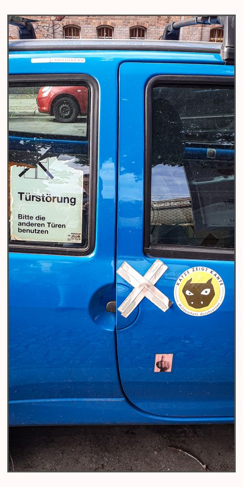 Foto eines blauen Kleinwagens. Auf der Seite des Fahrzeugs ist ein Schild mit der Aufschrift 