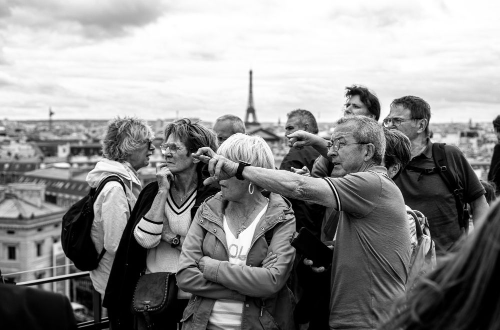 A black and white photo of a group of people pointing and looking in the opposite direction of Paris' famous Eiffel Tower