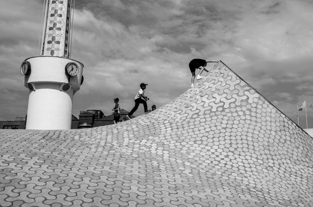 Children playing on a highly patterned surface, outlined against the sky. Black and white. 