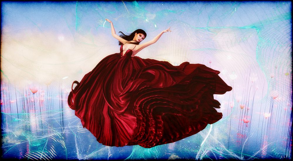 A digital screenshot from #secondlife features a female avatar in a flowing red dress, gracefully floating in mid-air as if dancing. The background is an abstract blend of blue tones, creating a dreamy, surreal atmosphere. The avatar's pose conveys elegance and movement, with the vibrant red of the dress standing out against the cool, ethereal backdrop.