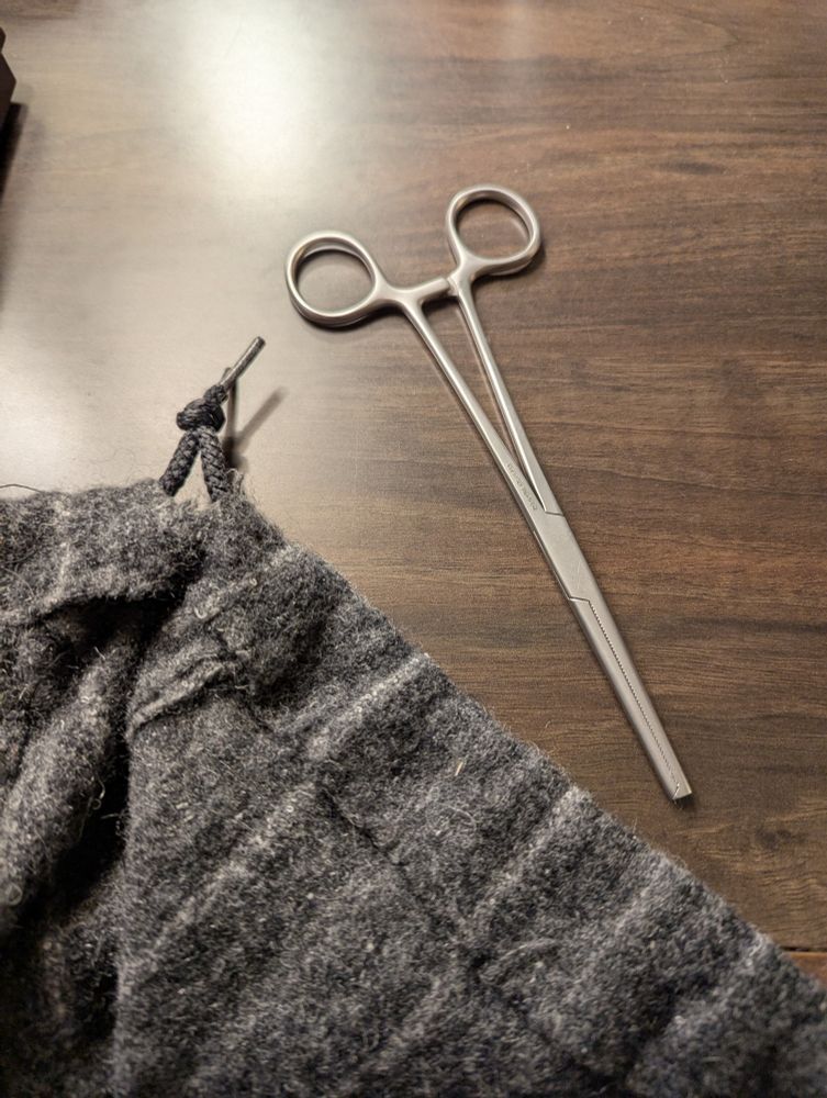 Wool fabric of roughly historically recreated pants with a set of forceps to the side.