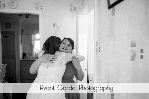 A black and white wedding photo of the two women hugging, one in a bridal gown and one in a bridesmaid dress.