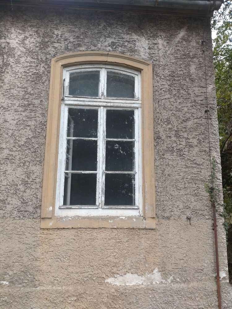 Sprossenfenster mit Oberlicht mit Segmentbogen von Ende 19. Jahrhundert. Der Lack platzt ab, das Holz ist morsch.