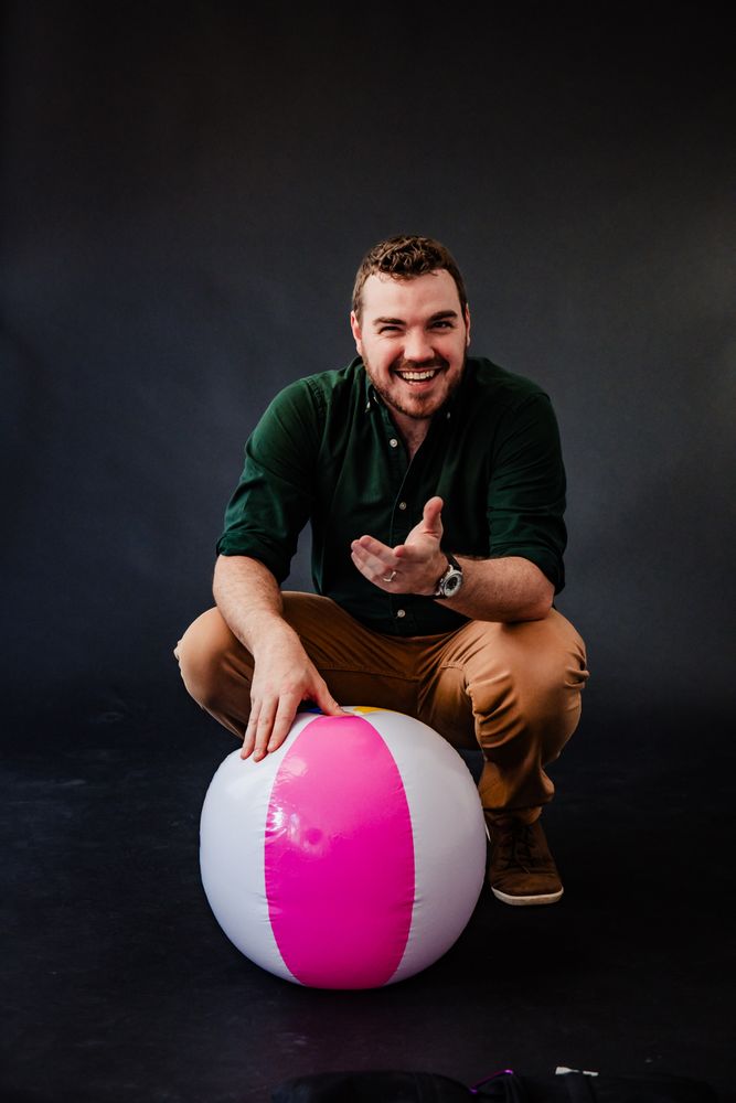 Duncan Leaning on a beach ball smiling and holding out a hand