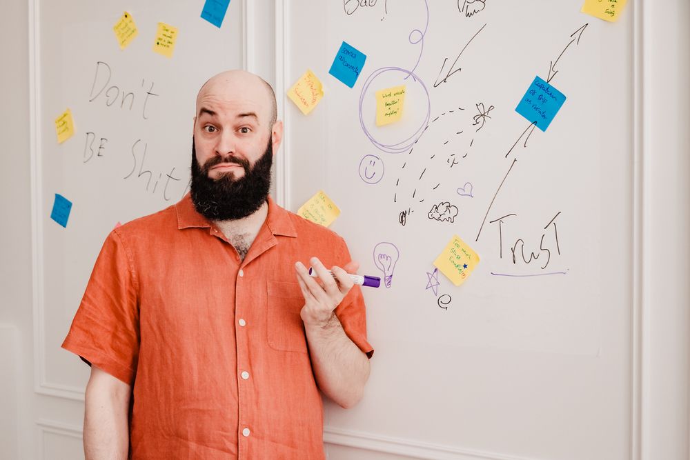 Matt stands in front of a wall covered in post it's and scribbles. 