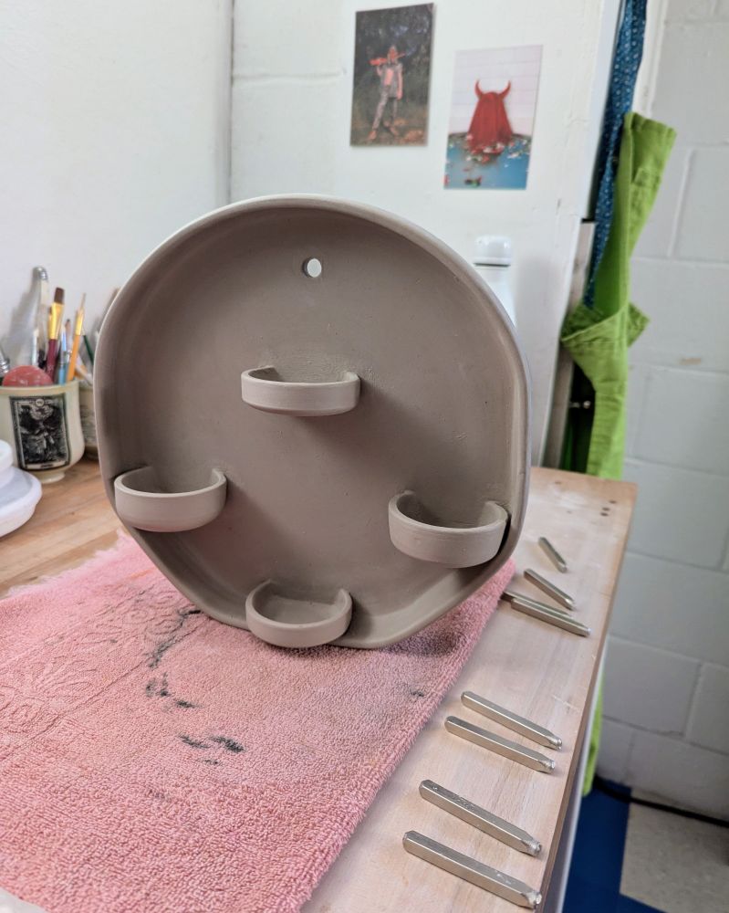 Photo of a large piece of wall hanging pottery. There are four shallow cups attached to hold tealights or votives or incense or whatever.