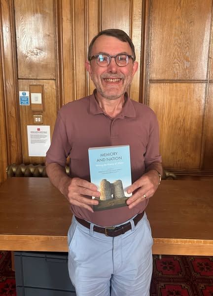 An image of Professor Huw Pryce holding a copy of the festschrift published in honour of him, 'Memory and Nation: Writing the History of Wales'.