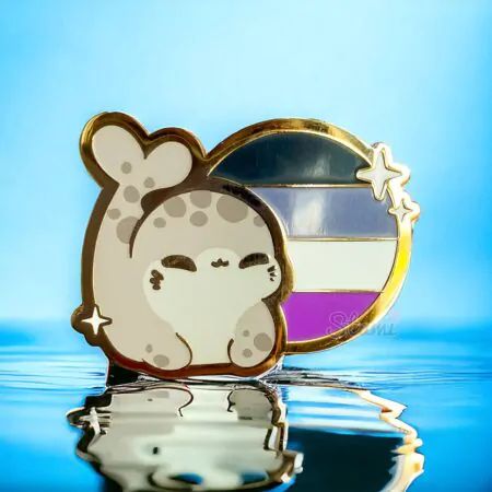 A photo of an enamel pin with a circular asexual flag design with a chibi art style grey spotted seal beside it. 