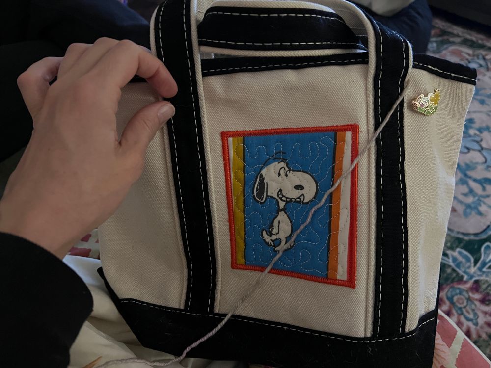 Little canvas tote bag with Snoopy patch. It also has a little enamel pin featuring Woodstock sleeping in a christmas wreath