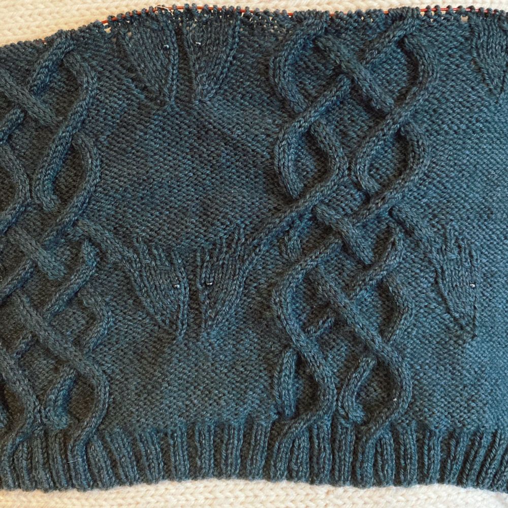 Knitted cables with dragon heads looking fierce with gunmetal grey beaded eyes. In a black watch green colour way 