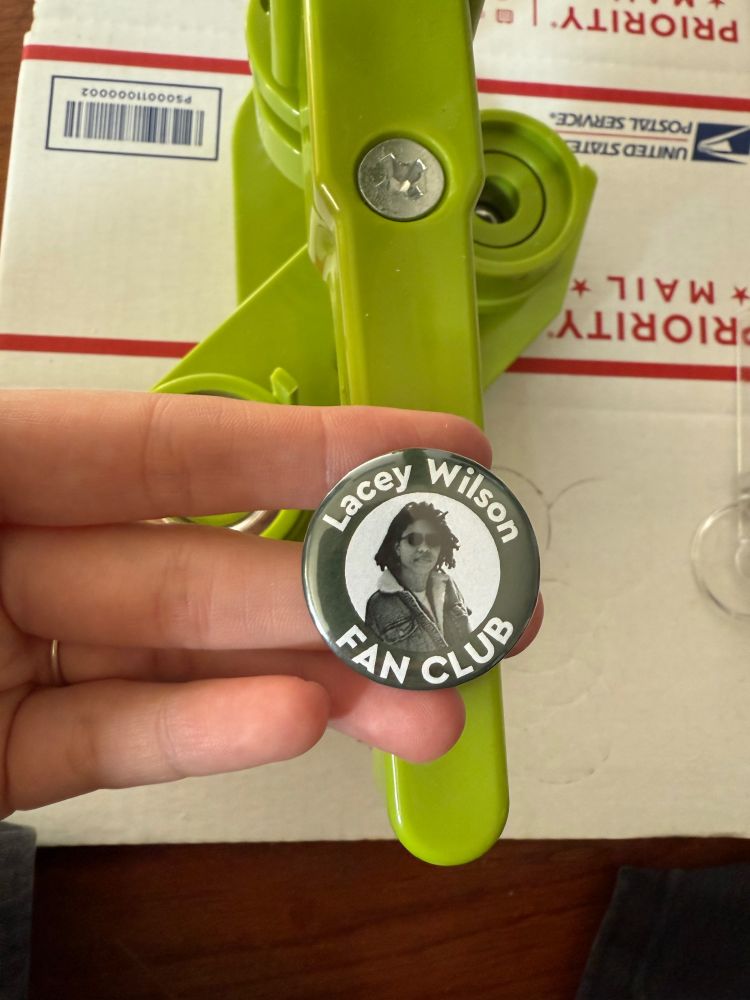 picture of a button maker in the background a button that says lacey wilson fan club in the foreground