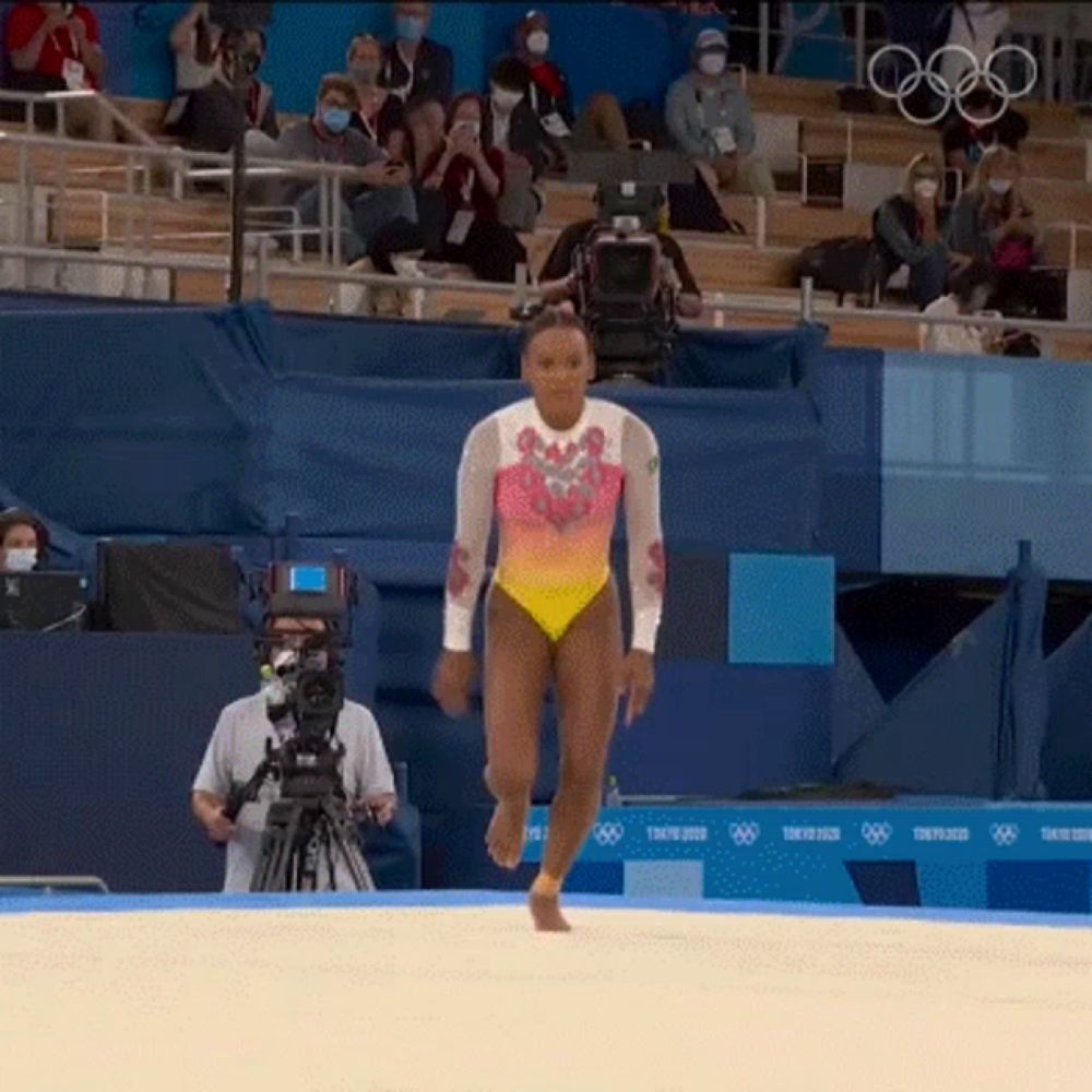 a woman in a leotard is walking on a sandy surface in front of a tokyo 2020 sign