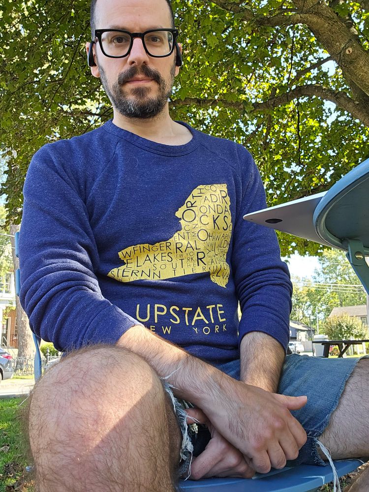 I'm sitting in the park on a sunny day, wearing jean shorts and a sweatshirt that says Upstate New York on the front because that's where I live. 